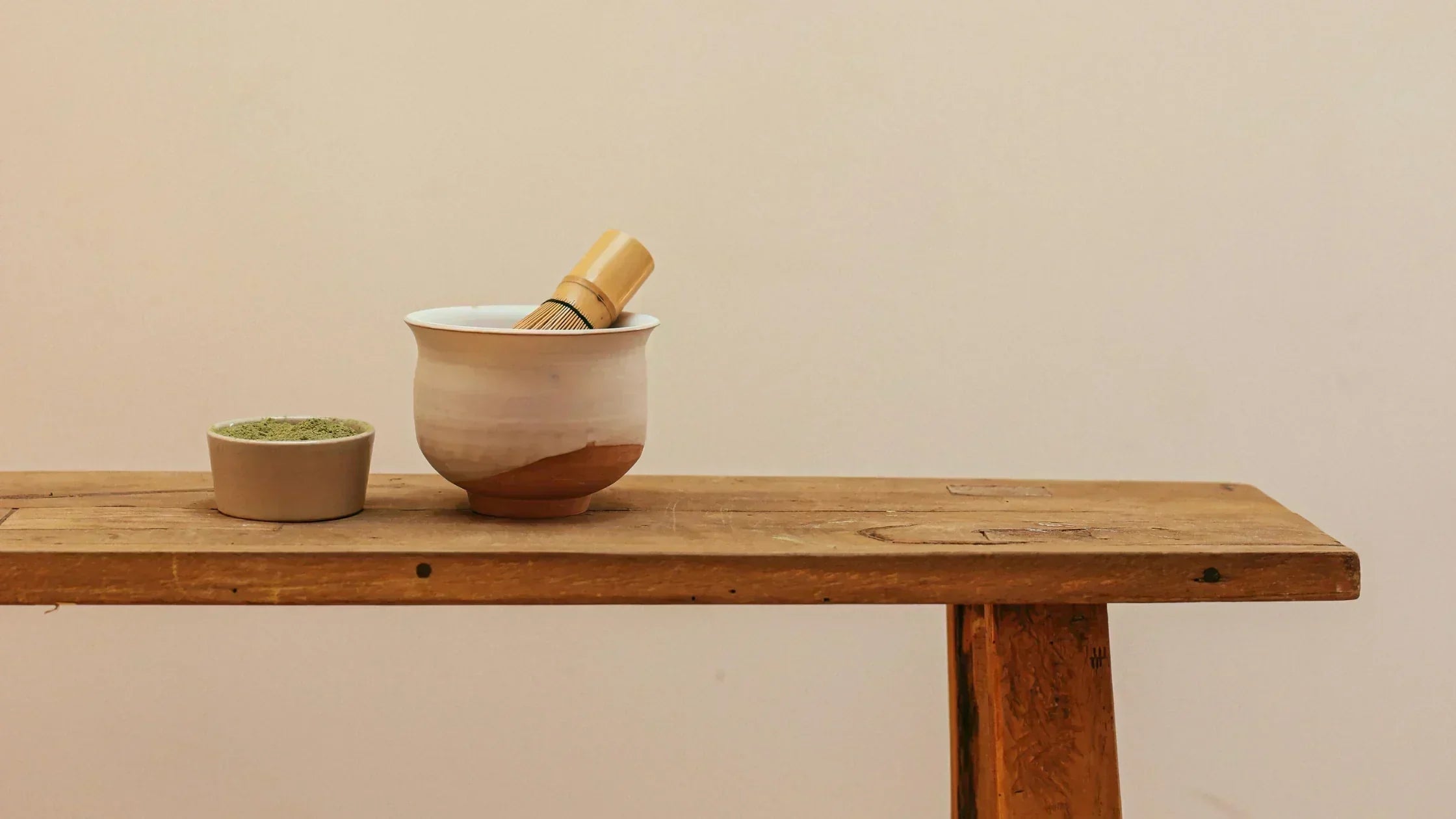 Bamboo whisk on a bowl next to a bowl of ceremonial grade matcha, ideal for traditional tea preparation.