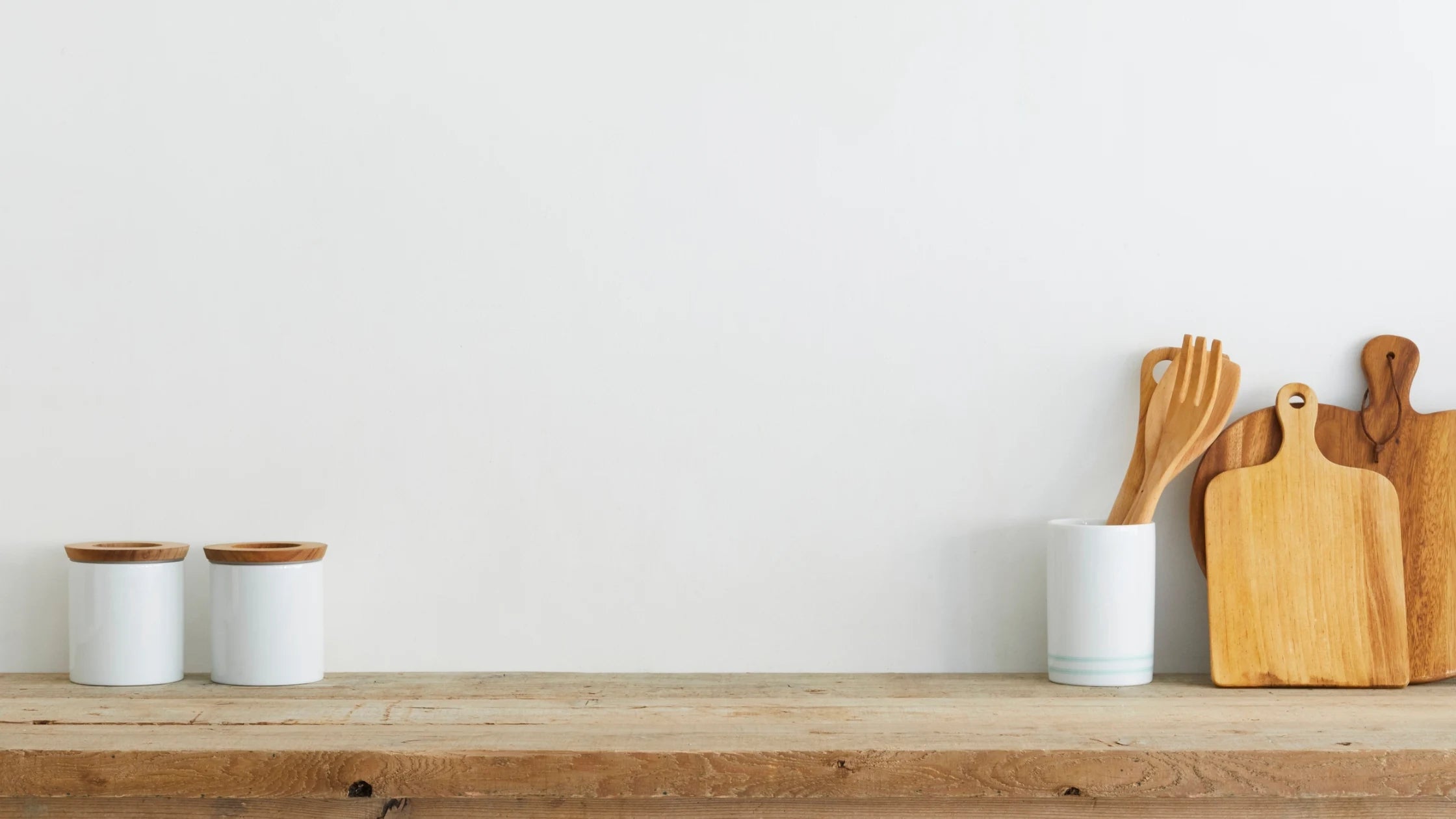 Wooden cutting boards and white containers on a wooden shelf against a white wall