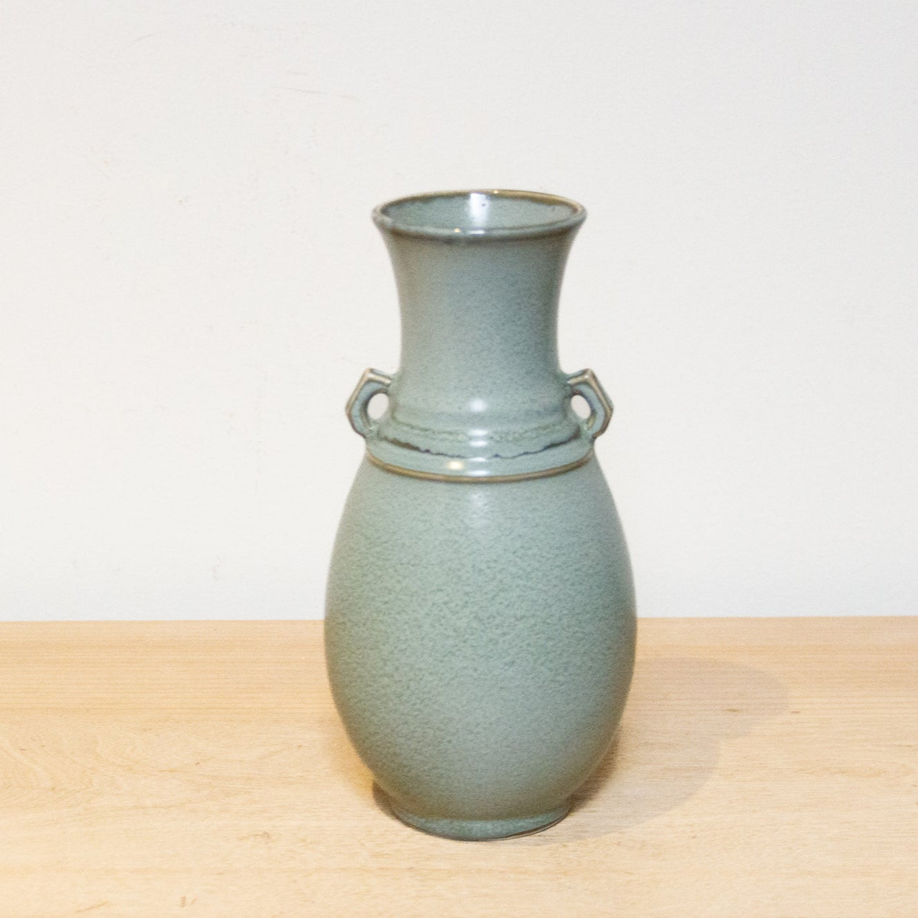 Green ceramic vase with ring handles on a light wooden surface and white background