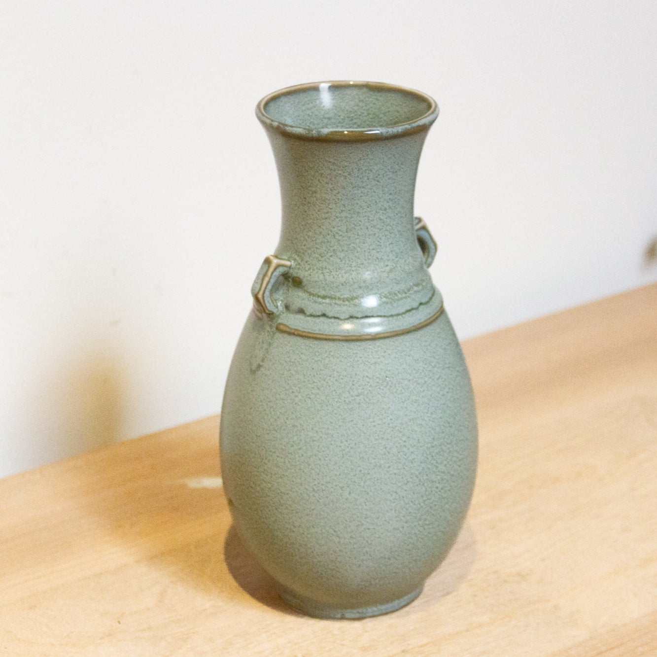 Green ceramic vase with ring handles on a wooden surface